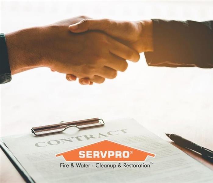 Two people shaking hands over a contract with a SERVPRO logo.