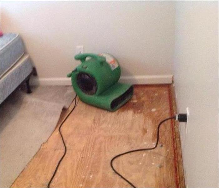 A green SERVPRO air mover set on plywood to dry the wet flooring after a water damage.